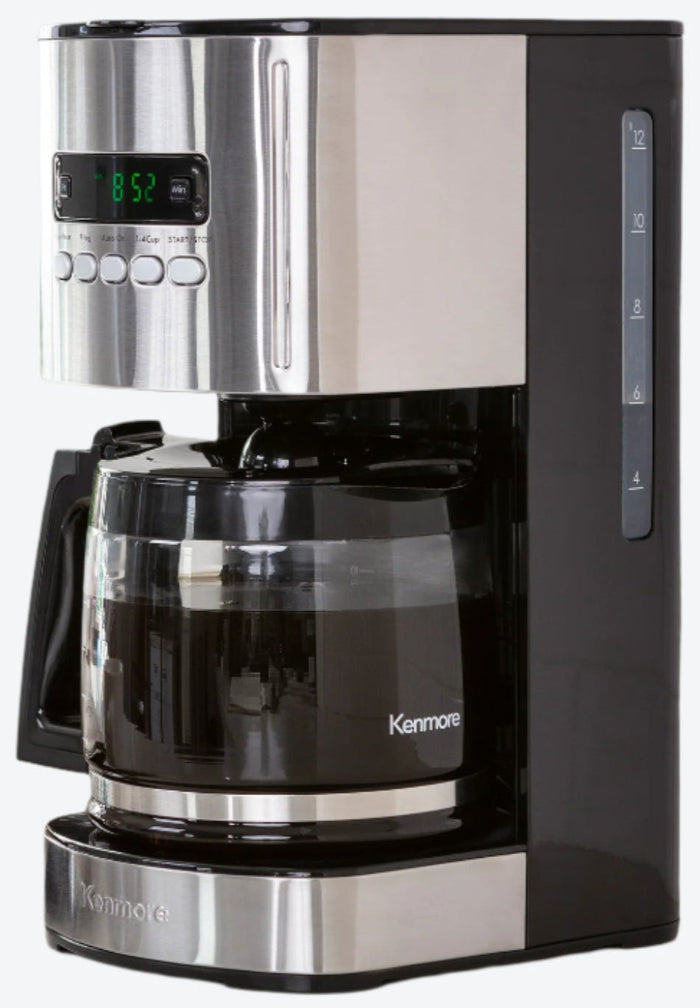 Kenmore 12 cup programmable coffeemaker on a light gray countertop with white tile backsplash behind and a mug, bag of coffee beans, and potted plant beside it