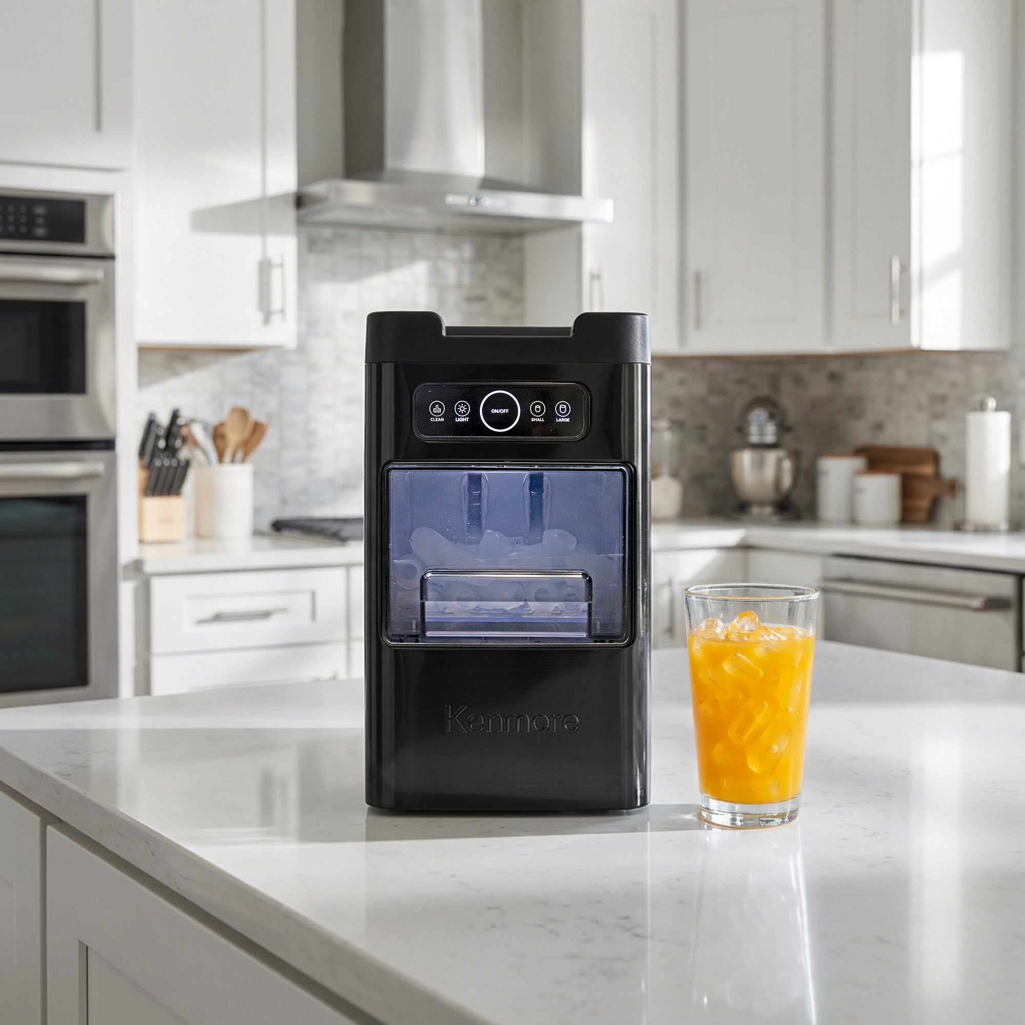 Kenmore front-load bullet ice maker on a white marble countertop with a glass of orange juice with ice to the right