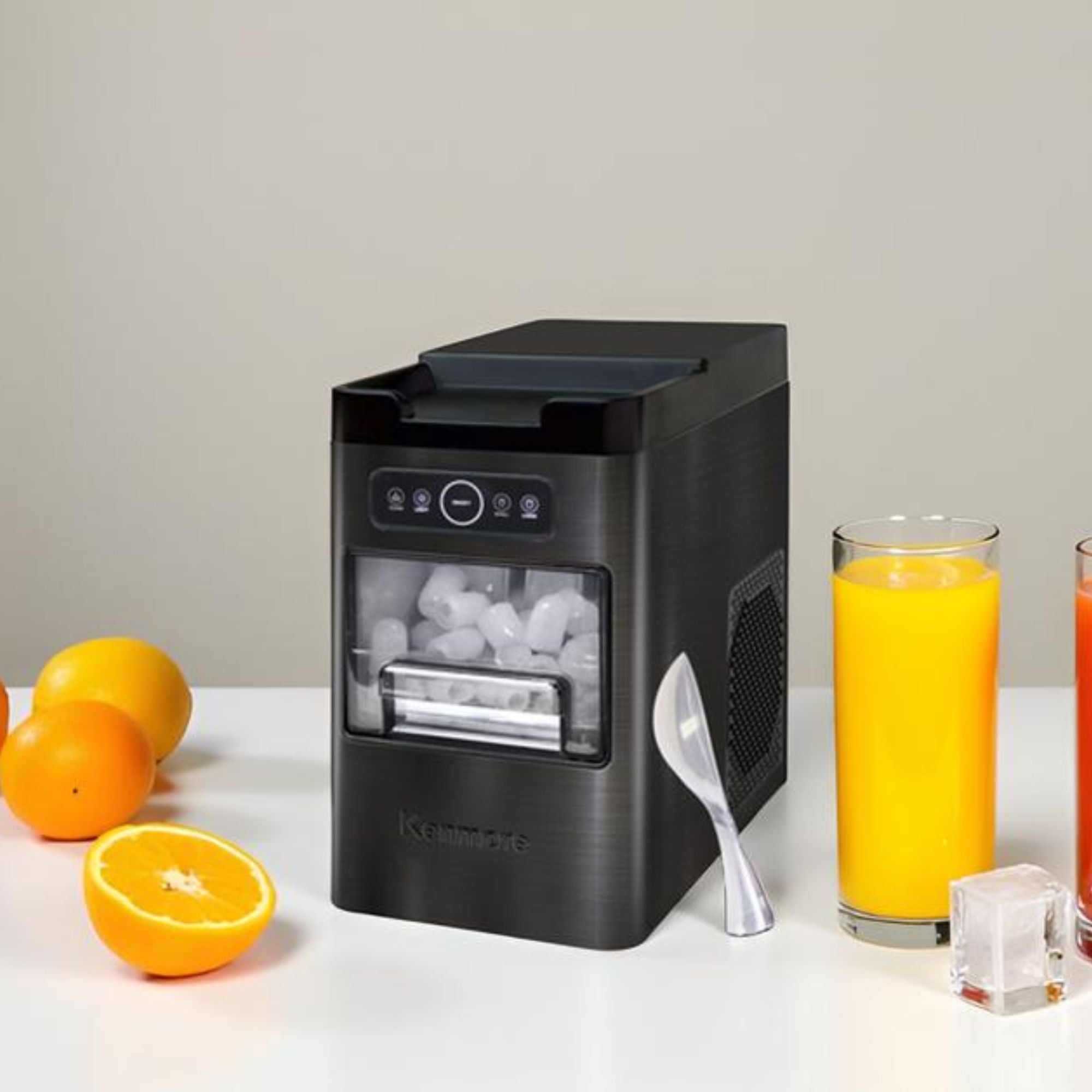 Kenmore automatic front-load ice maker on a white counter with oranges and a glass of orange juice arranged around it