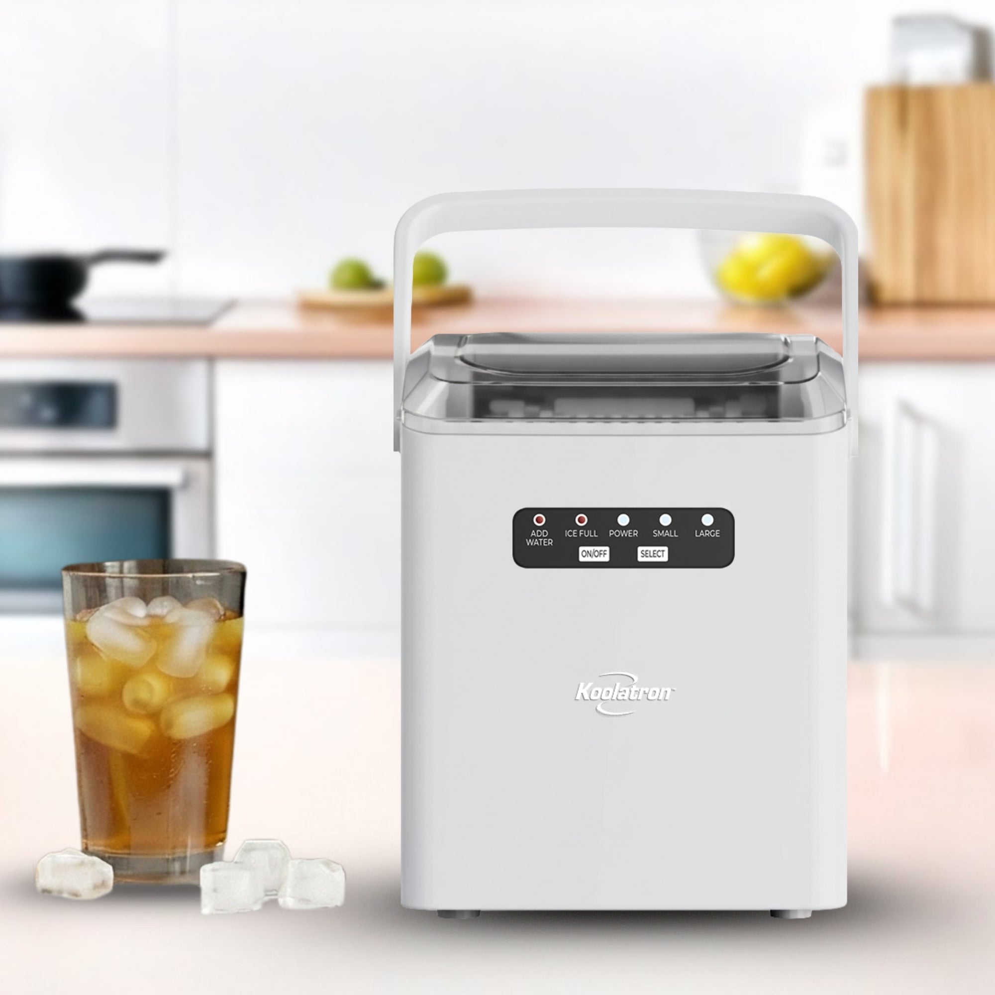 Automatic ice maker on a white countertop in a bright kitchen with an iced drink beside it