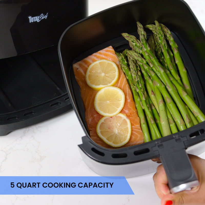 Closeup of air fryer basket containing a piece of salmon topped with lemon slices and a bunch of asparagus spears. Text below reads, 5 quart cooking capacity.